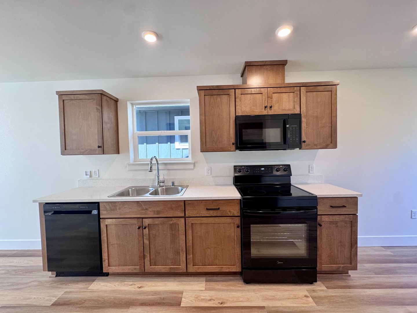 Kitchen with wood cabinets, black appliances, and quartz-look counters, straight-on view
